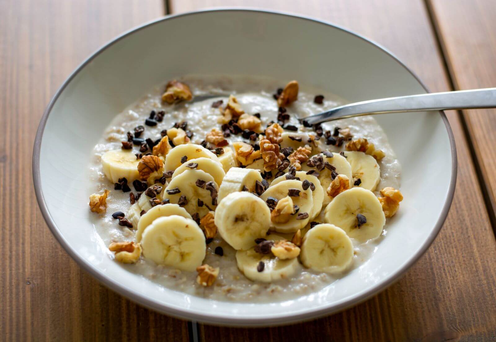 Un'immagine del porridge di avena guarnito con banane e mandorle, in una ciotola luminosa, su sfondo neutro